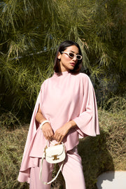 Woman in a pink outfit holding a white handbag with greenery in the background